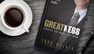 Coffee cup next to a book titled Greatness